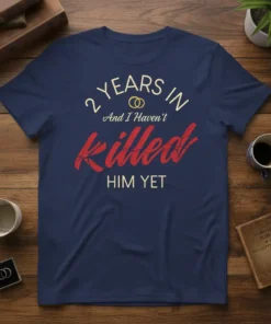 T-shirt with "2 Years In And I Haven't Killed Him Yet" text in cream and red, featuring wedding rings graphic