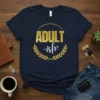 Navy t-shirt with "ADULT-ish" text in gold glitter and white script, framed by a gold laurel wreath