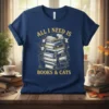 All I Need Is Books & Cats text design on a navy blue t-shirt, featuring a stack of books with