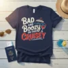 Navy blue t-shirt with white and red text reading "BAD AND Boozy ON THIS Cruisey," featuring a cartoon cruise ship