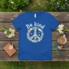 Blue t-shirt with "Be kind" text above a colorful floral peace symbol design featuring birds and butterflies