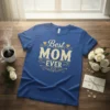 Blue t-shirt with "Best MOM EVER" text in gold, featuring decorative elements and a polka dot pattern within the letters