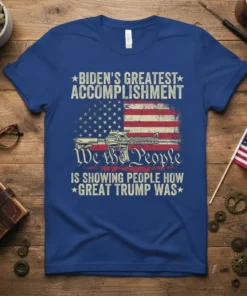 Political t-shirt with American flag graphic, rifle, and text "Biden's Greatest Accomplishment We the People Is Showing People How Great