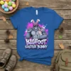 Bigfoot wearing bunny ears and holding a baby bunny, with text "BIGFOOT EASTER BUNNY" on a blue t-shirt