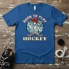 Born to Play Hockey text with crossed hockey sticks, helmet, and puck graphic on a blue t-shirt
