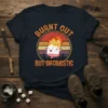 Burnt Out But Optimistic text with a flaming marshmallow graphic on a dark t-shirt