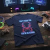Navy t-shirt with neon blue text "CAN'T HEAR YOU YOU'RE GLITCHING" and a red controller with headphones graphic