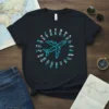 Black t-shirt with a cyan geometric airplane graphic and circular text listing aviation terms, including the phrase "CATCH YOUR DREAMS"