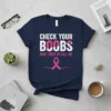Navy blue t-shirt with white and pink text reading "CHECK YOUR BOOBS MINE TRIED TO KILL ME" and a pink