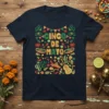 Cinco de Mayo text surrounded by festive Mexican graphics including cacti, sombreros, chili peppers, and maracas on a navy t-shirt