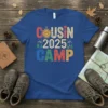 COUSIN 2025 CAMP text graphic with a smiling sun, mountains, and trees on a blue t-shirt