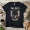 Black t-shirt featuring "I'm a Crazy Childless Cat Lady" text with a black cat wearing an American flag bandana and