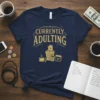 Currently Adulting funny quote t-shirt design with graphics of a trash can overflowing with adult responsibilities