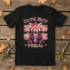 Cute But Feral red panda t-shirt design with pink accents and a stylized drink, featuring the text "CUTE BUT FERAL"