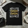Black t-shirt with "DADA DADA" in gold glitter text, surrounded by abstract white geometric shapes and faces, representing Dada art