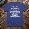 Daddy's Little Mechanic In Training text with piston and wrench graphics on a blue t-shirt