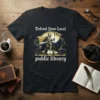 Defend Your Local Public Library t-shirt design with a knight riding a black cat, featuring gothic font and a golden
