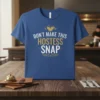 T-shirt with the text "Don't Make This Hostess Snap" in white and gold, featuring a cracked coffee cup graphic