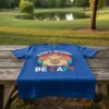 Blue t-shirt with "Don't Worry Be Capy" text and a cute capybara graphic in a retro sunset circle