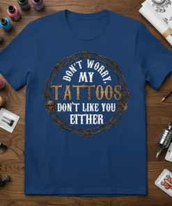 Blue t-shirt with "DON'T WORRY, MY TATTOOS DON'T LIKE YOU EITHER" text inside a barbed wire circle, featuring skulls