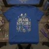 Blue t-shirt with "HAIR STYLIST" in gold glitter font, bunny ears, scissors, comb, hairdryer, and Easter eggs
