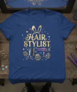 Blue t-shirt with "HAIR STYLIST" in gold glitter font, bunny ears, scissors, comb, hairdryer, and Easter eggs