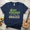 Eat Avocados And Play The Ukulele text design with avocado and ukulele graphics on a navy t-shirt