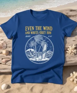 Christian t-shirt with golden text "EVEN THE WIND AND WAVES OBEY HIM MARK 4:41 Be Still" above a beach scene