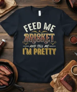Black t-shirt with "Feed Me Brisket And Tell Me I'm Pretty" text in vintage distressed font, celebrating BBQ and brisket