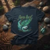 Dark navy t-shirt with a green and gold "fern leaf" graphic featuring stylized waves and a fern frond