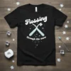 Black t-shirt with white text "Flossing through the snow" and crossed blue toothbrushes with snowflakes