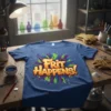 The phrase "Frit HAPPENS!" in bold, colorful graffiti-style text on a blue t-shirt, representing glass fusing art