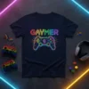 GAYMER text in neon rainbow colors above a glowing video game controller with circuit board details, dark navy t-shirt