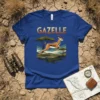 Gazelle text above a leaping gazelle graphic on a blue t-shirt, set against an African savanna landscape with acacia trees