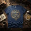 Vintage style t-shirt with gold text "GETTING OLD SUCKS" inside a wreath with gears and hourglass