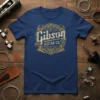 Gibson Guitar Co. vintage logo text design on a navy blue t-shirt, featuring ornate golden embellishments