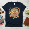 Navy t-shirt featuring the word "Gigi" in a retro font within a colorful heart mandala, surrounded by flowers and peace
