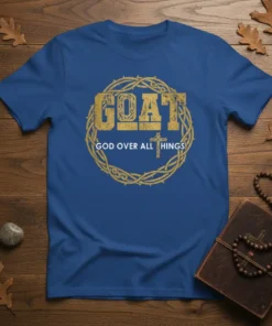 Blue t-shirt with distressed gold text "GOAT" and "GOD OVER ALL THINGS" within a thorn wreath and cross graphic