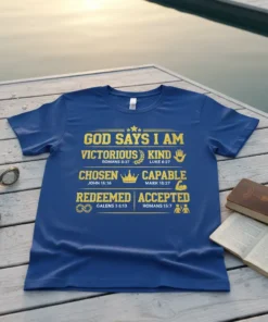 Blue t-shirt with gold text listing affirmations: God Says I Am Victorious, Kind, Chosen, Capable, Redeemed, Accepted, with scripture references