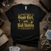 Black t-shirt with "Good Girl with Bad Habits" text in gold gothic font, featuring martini glass and smoking lips graphics