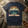 Good Lord Willing and the Creek Don't Rise quote on a navy t-shirt featuring a retro mountain and creek landscape