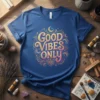 Good Vibes Only quote in ornate gold and pink lettering on a blue t-shirt, with celestial accents like moons and
