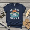 Guess What Week It Is text with a cool shark wearing sunglasses surfing a wave, vintage sunset graphic on a