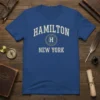 Hamilton New York text design on a royal blue t-shirt with a shield logo and 'H'