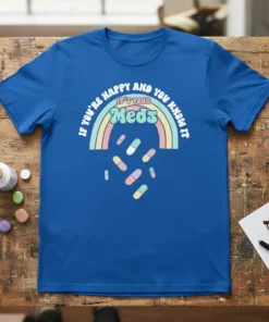 Blue t-shirt with "If You're Happy And You Know It It's Your Meds" text and rainbow design with falling pills