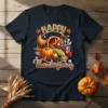 Happy Thanksgiving text above a cornucopia filled with pumpkins, grapes, corn, and apples, on a navy t-shirt