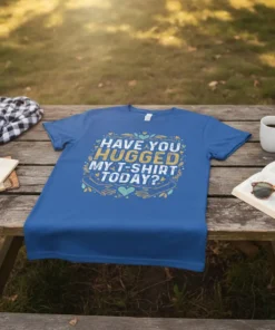 Text design "Have You Hugged My T-Shirt Today?" with floral accents and hands embracing on a blue t-shirt