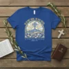 Blue t-shirt with "HE IS NOT HERE. HE HAS RISEN. Matthew 28:6" text and sunrise cross graphic