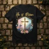 He is Risen Christian T-Shirt featuring a golden cross, a silhouette of a rider on a donkey, and floral accents