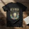 He Is Risen Christian Easter T-Shirt with empty tomb, cross, lilies, and butterflies graphic